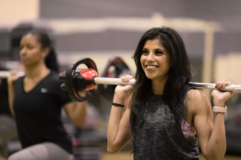 Woman smiling lifting weights during small group training